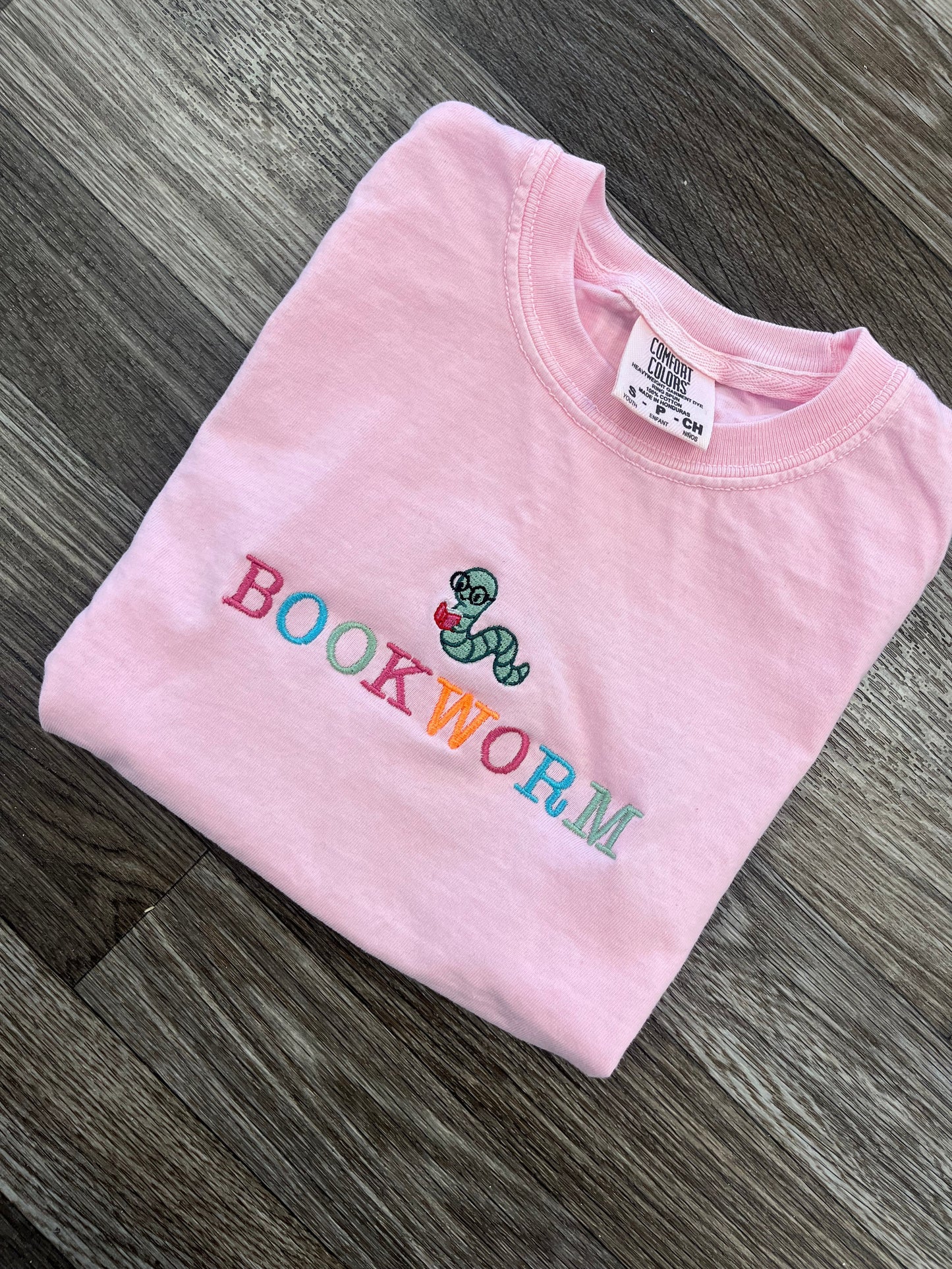 Pink t-shirt with 'bookworm' design on a wooden surface