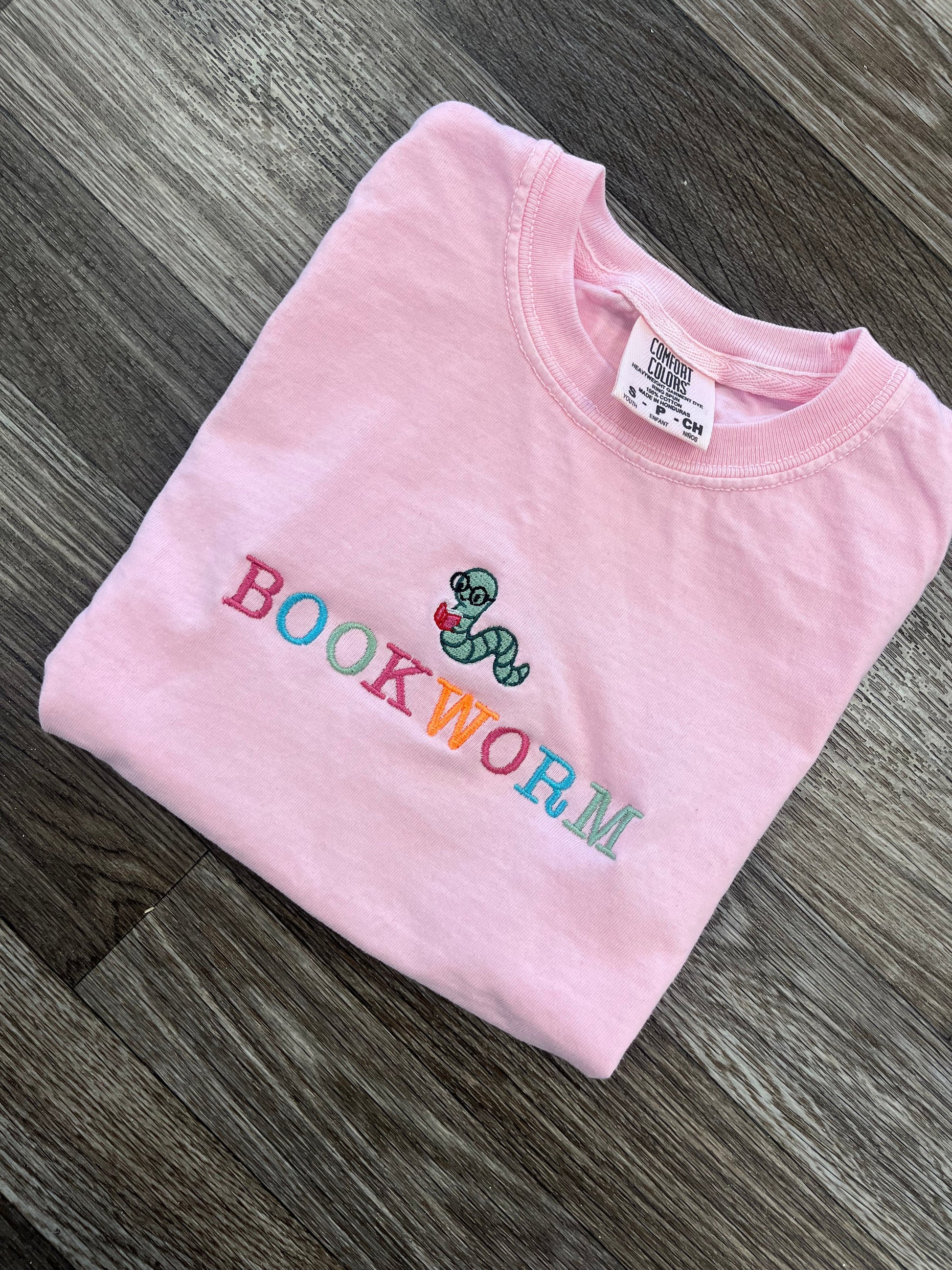 Pink t-shirt with 'bookworm' design on a wooden surface
